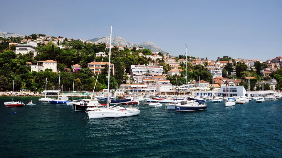 Sailboats moored off a Dubrovnik waterfront backed by green hills.
