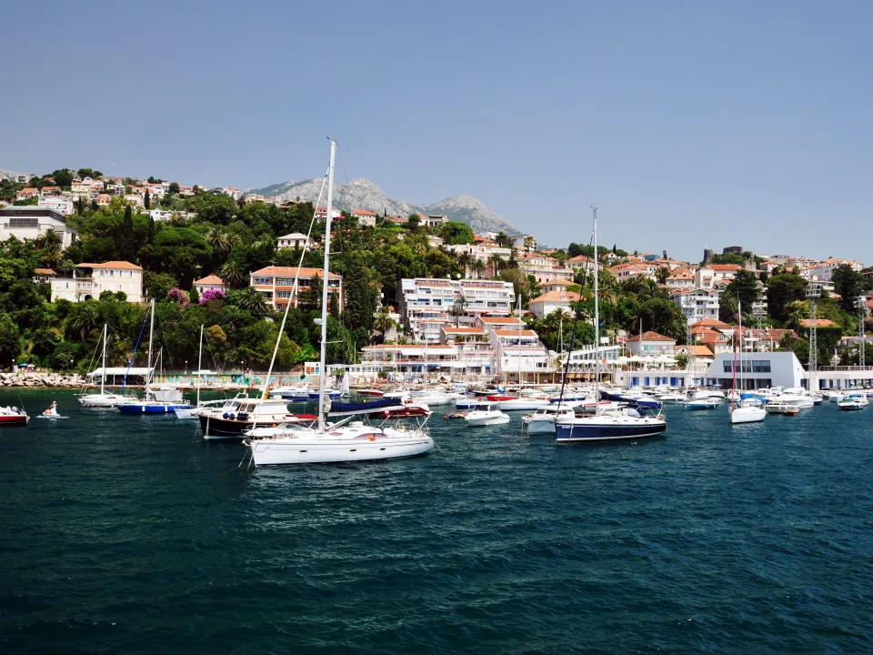 Sailboats moored off a Dubrovnik waterfront backed by green hills.