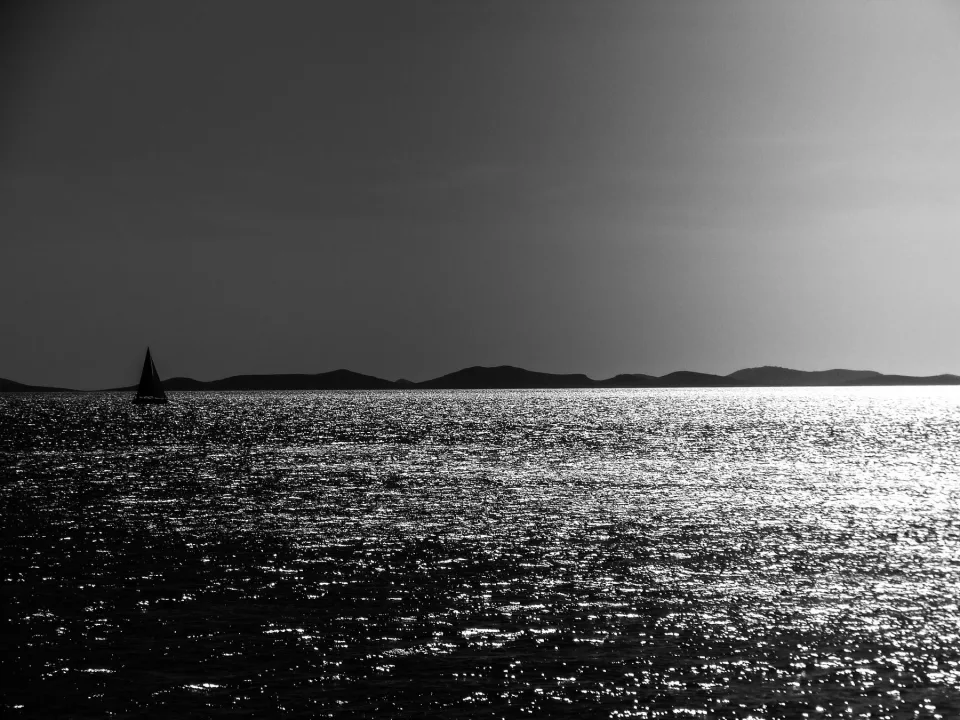 A sailboat off Murter in a black and white seascape.