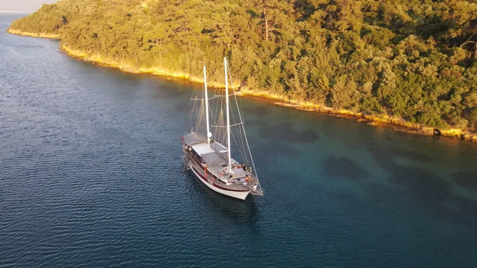 Wooden gulet moored beside a wooded Mediterranean coast.