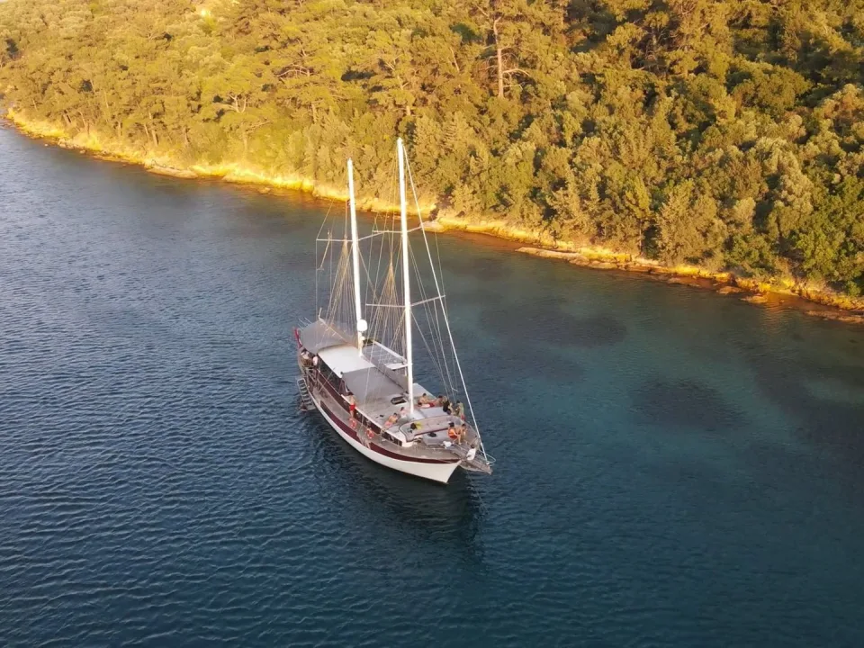 Wooden gulet moored beside a wooded Mediterranean coast.