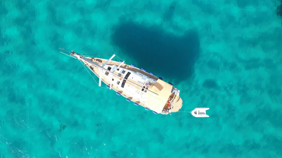A sailing yacht and its tender viewed from above in turquoise water off Porto Cervo, Sardinia