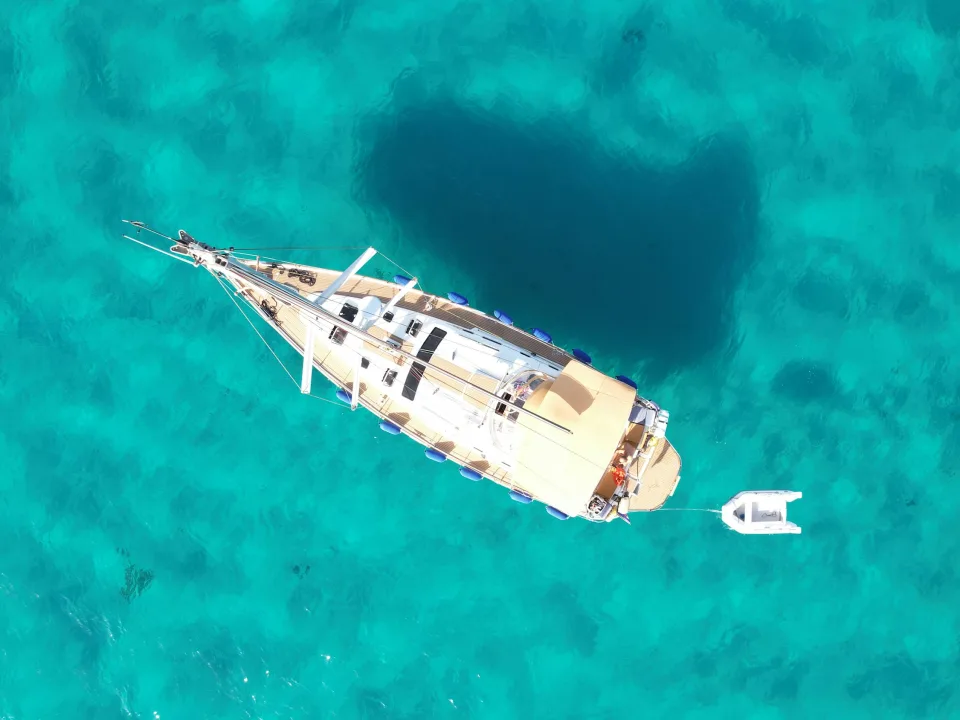 A sailing yacht and its tender viewed from above in turquoise water off Porto Cervo, Sardinia