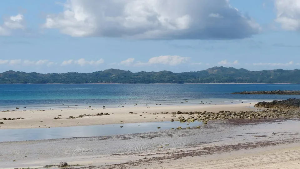 Sandy and rocky shore with blue water and clouds on Nosy Be, Madagascar
