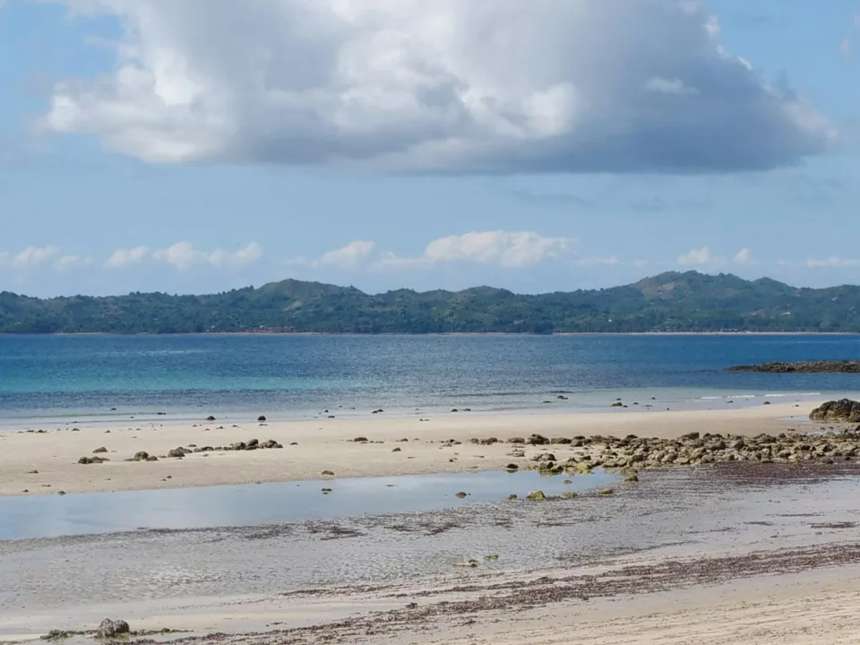 Sandy and rocky shore with blue water and clouds on Nosy Be, Madagascar