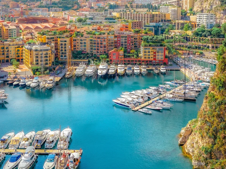 Boats moored in a Monaco harbour beneath colourful waterfront buildings and a wooded hillside