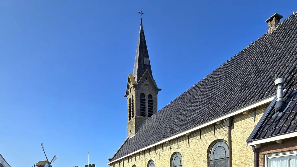 Sint-Michael church spire and brick walls under blue sky in Woudsend