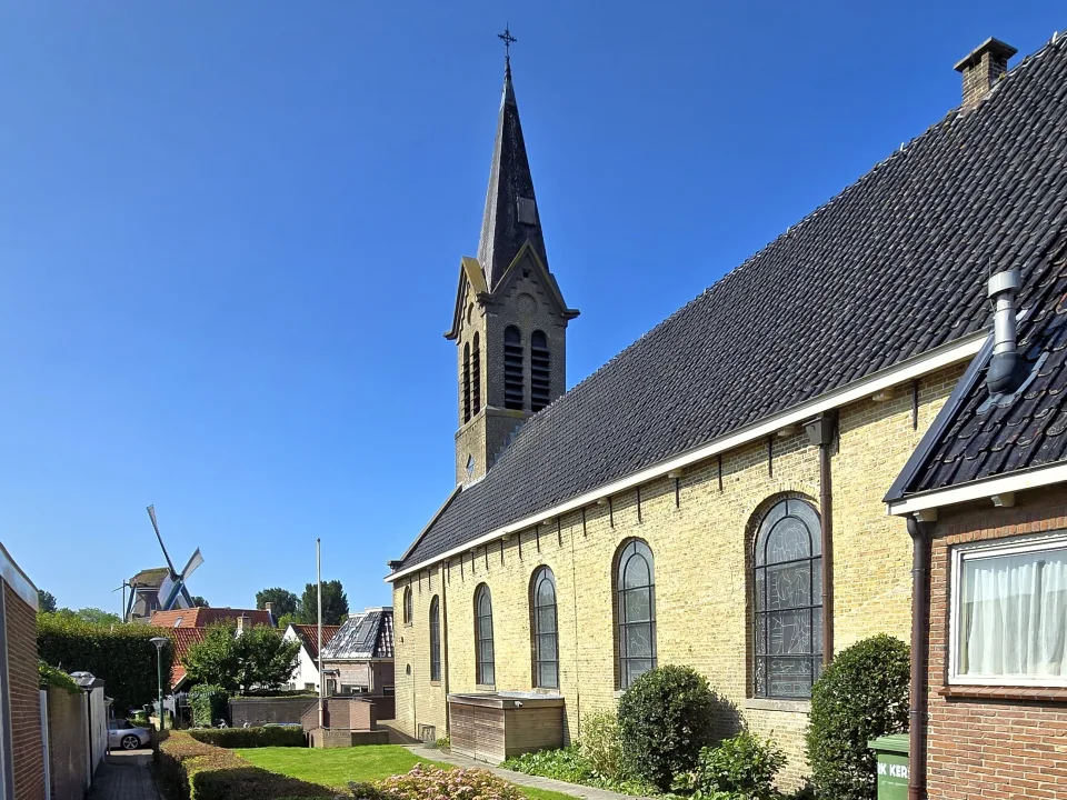 Sint-Michael church spire and brick walls under blue sky in Woudsend