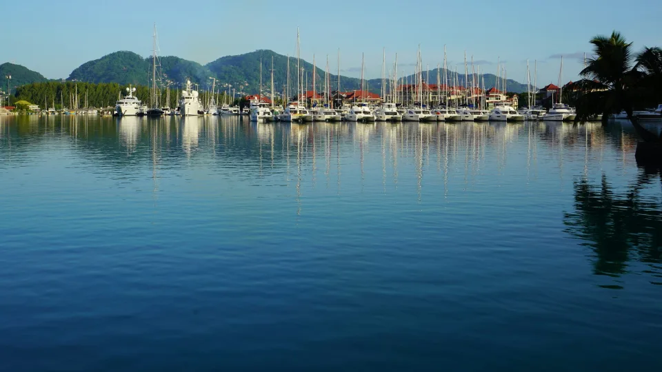 Regional marina context: moored yachts and waterfront buildings at Eden Island on Mahé, with hills and reflections