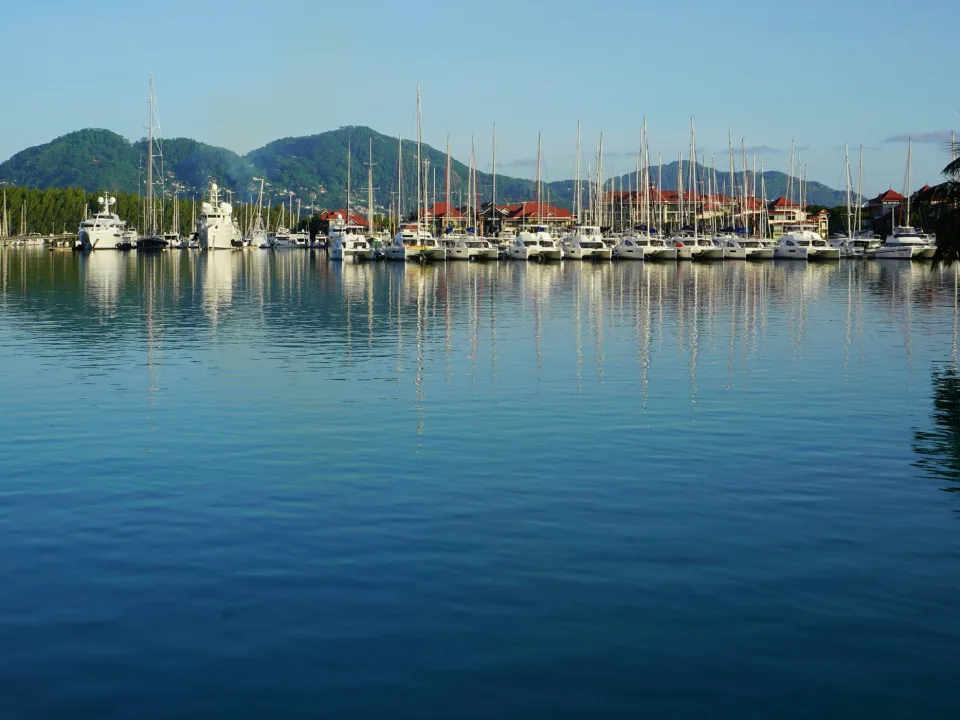 Regional marina context: moored yachts and waterfront buildings at Eden Island on Mahé, with hills and reflections