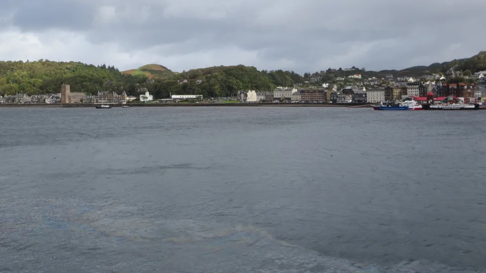 Regional harbour context: the Oban waterfront and wooded hills across grey bay water