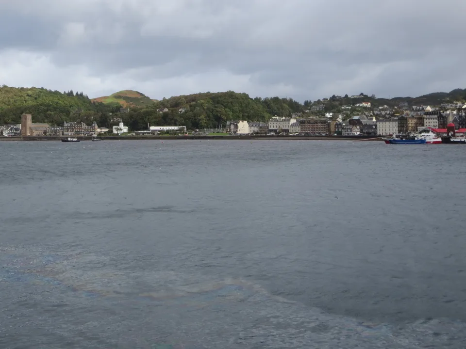 Regional harbour context: the Oban waterfront and wooded hills across grey bay water