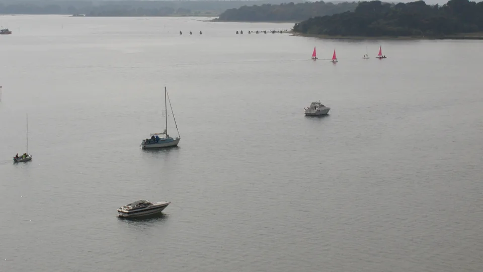 Regional harbour context: small sailing and motor boats in Poole Harbour, with wooded shoreline and hazy hills