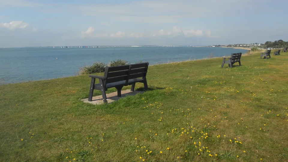The Solent shoreline at Lee-on-the-Solent, with blue water, distant sails and grassy seafront benches