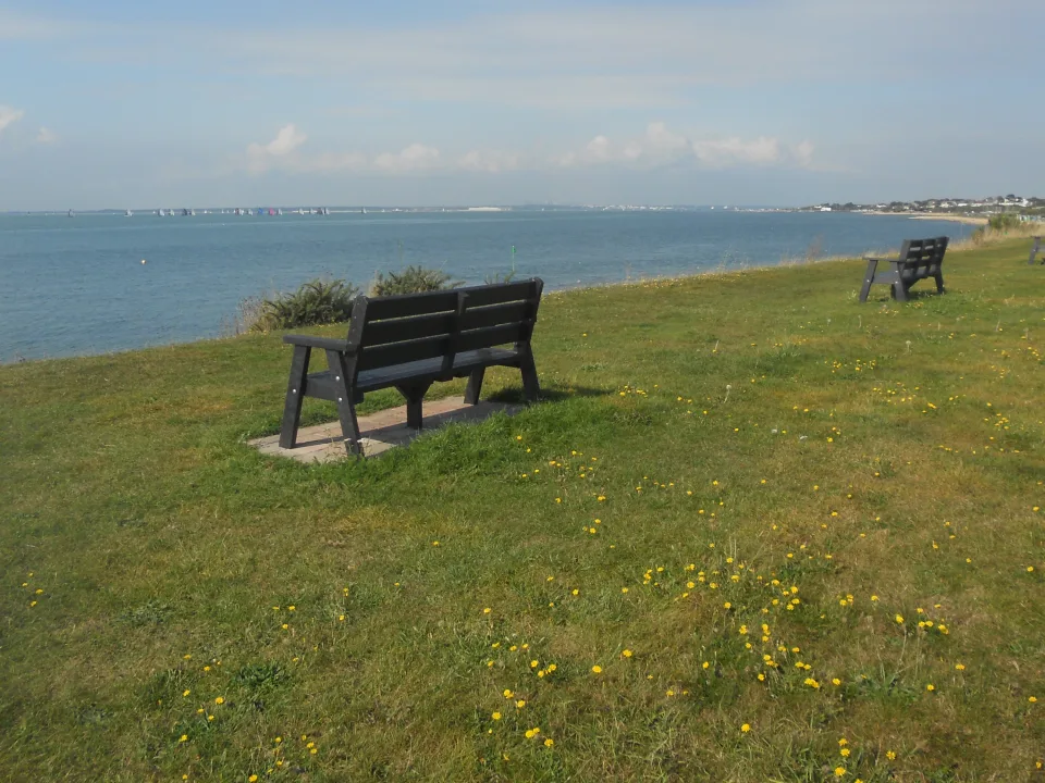 The Solent shoreline at Lee-on-the-Solent, with blue water, distant sails and grassy seafront benches