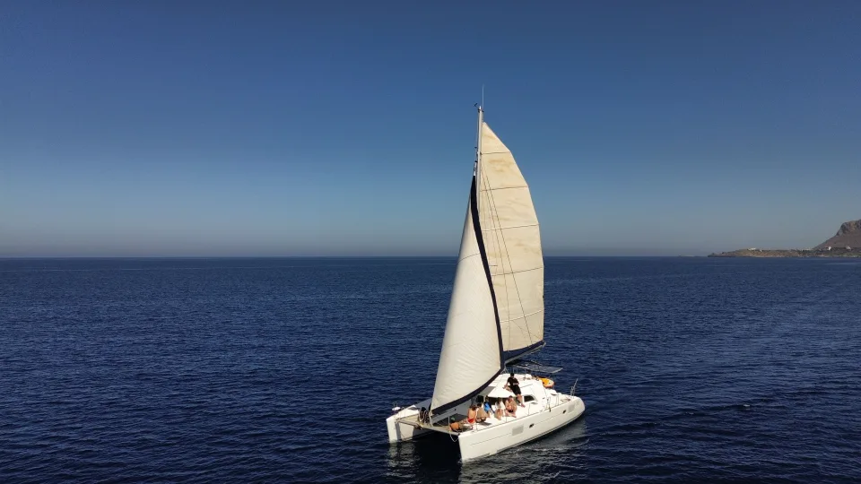 A sailing catamaran with twin hulls and raised sails on open water.