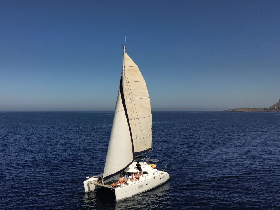 A sailing catamaran with twin hulls and raised sails on open water.