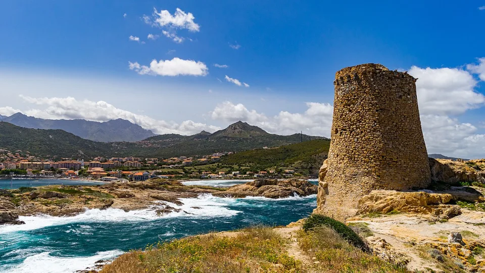 A stone coastal tower above waves and the rocky shore of Corsica.