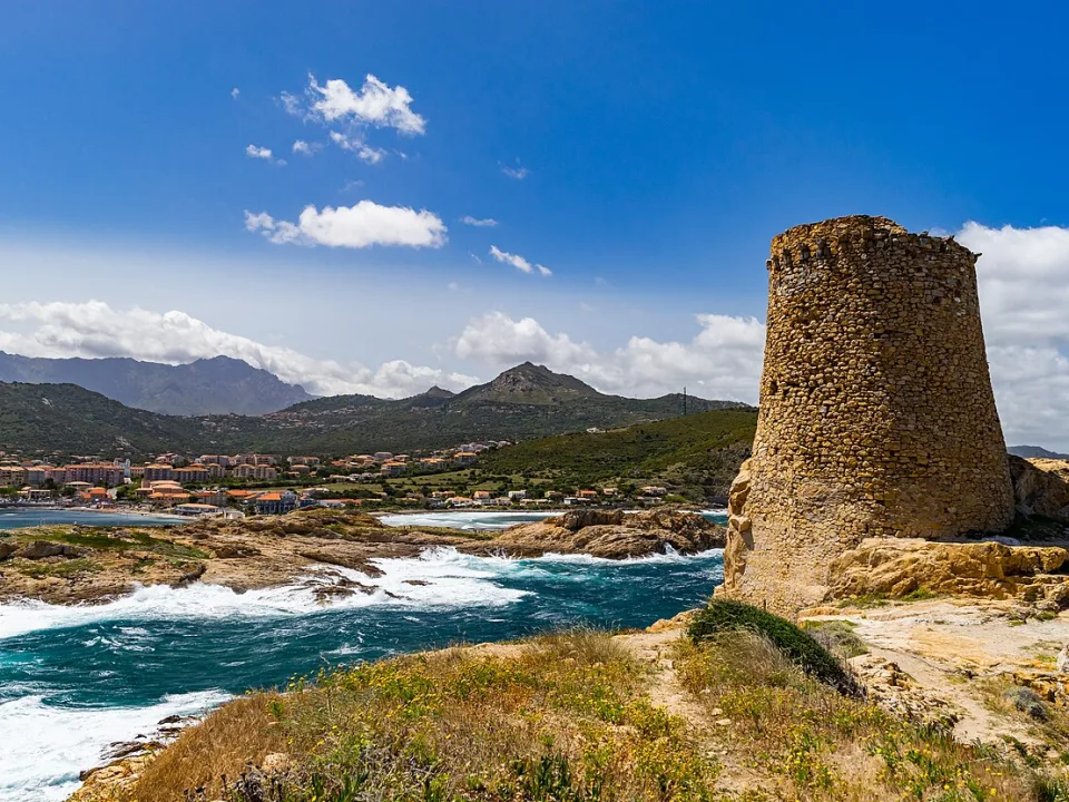 A stone coastal tower above waves and the rocky shore of Corsica.
