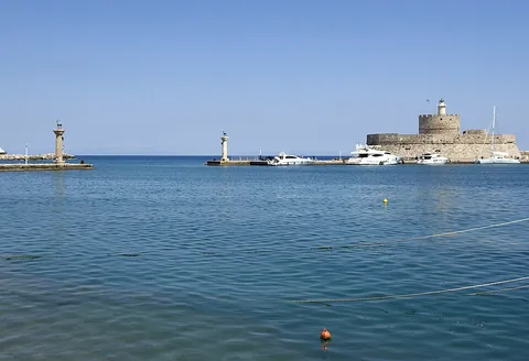 Входът на пристанище Мандраки на Родос с каменна крепост и лодки.