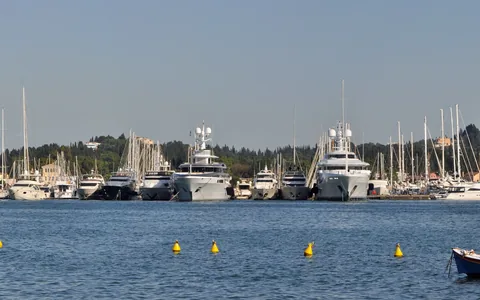 Яхти в марина Гувия на фона на зелени хълмове, погледнати откъм водата.