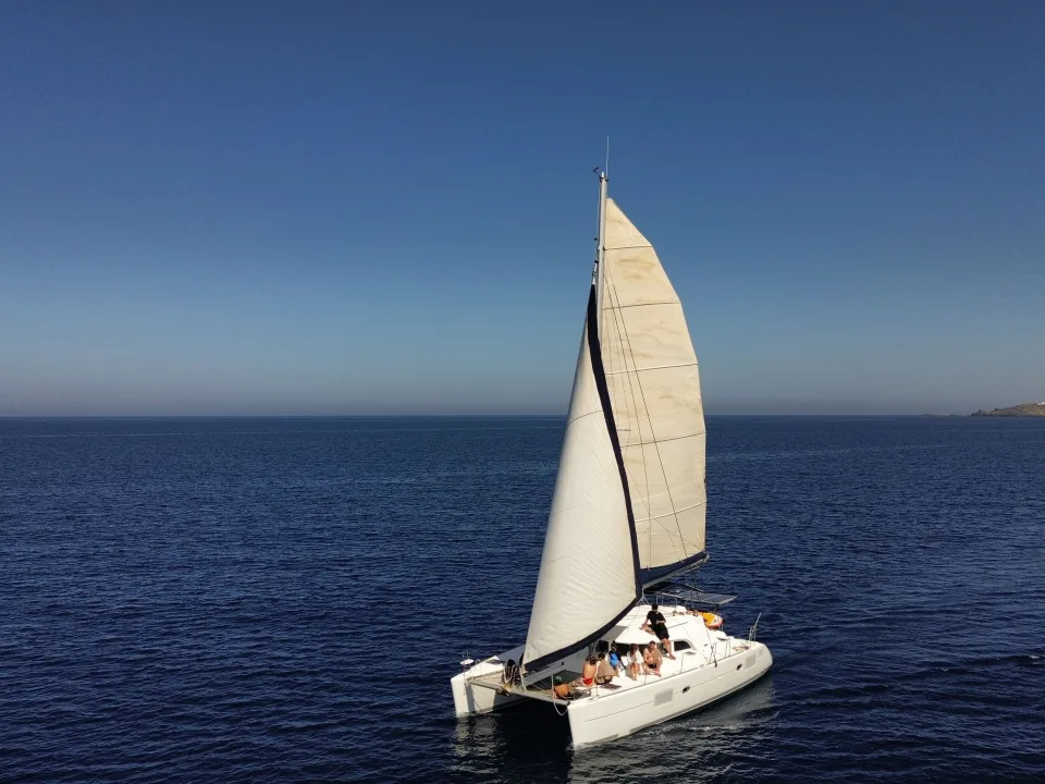 A sailing catamaran with twin hulls and raised sails on open water.