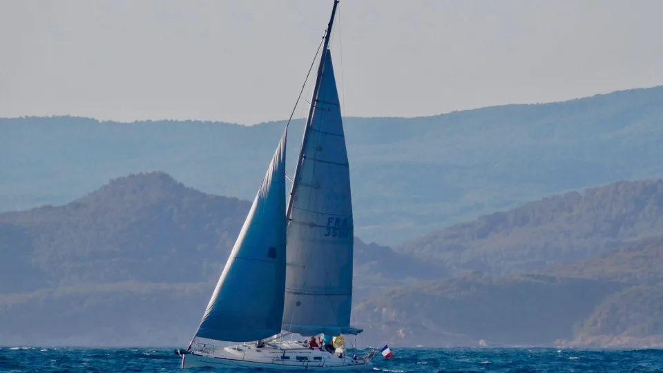 A sailing monohull yacht with two sails raised on blue water.