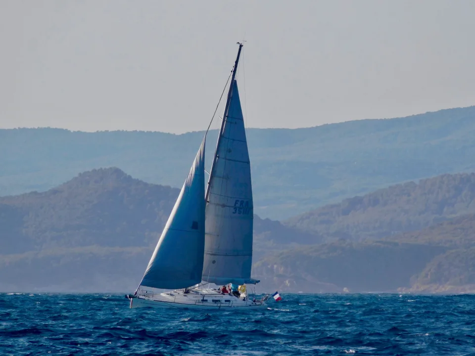A sailing monohull yacht with two sails raised on blue water.